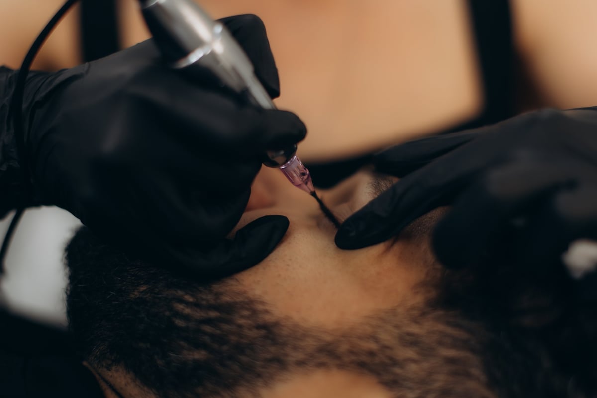 Professional artist applying micropigmentation on a man's head, creating a natural-looking hairline effect in a beauty salon